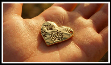 Gold heart charm engraved with eyes in an open palm