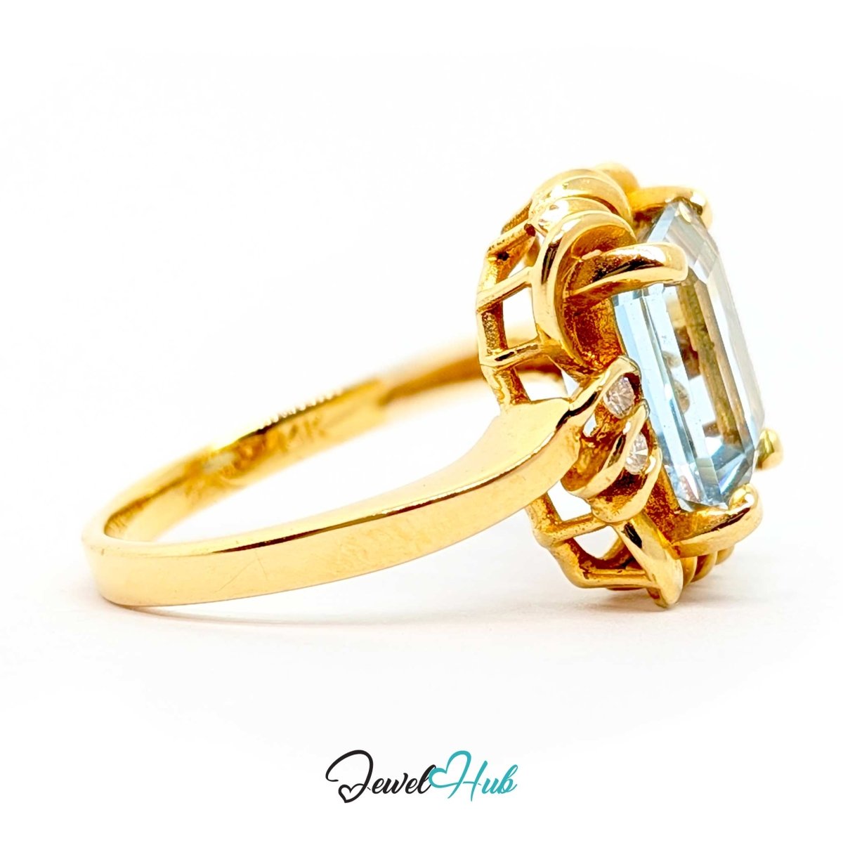 A 14k yellow gold ring featuring a large, rectangular emerald-cut light blue gemstone in an ornate openwork setting, shown on a clean white background with a 'JewelHub' watermark at the bottom.