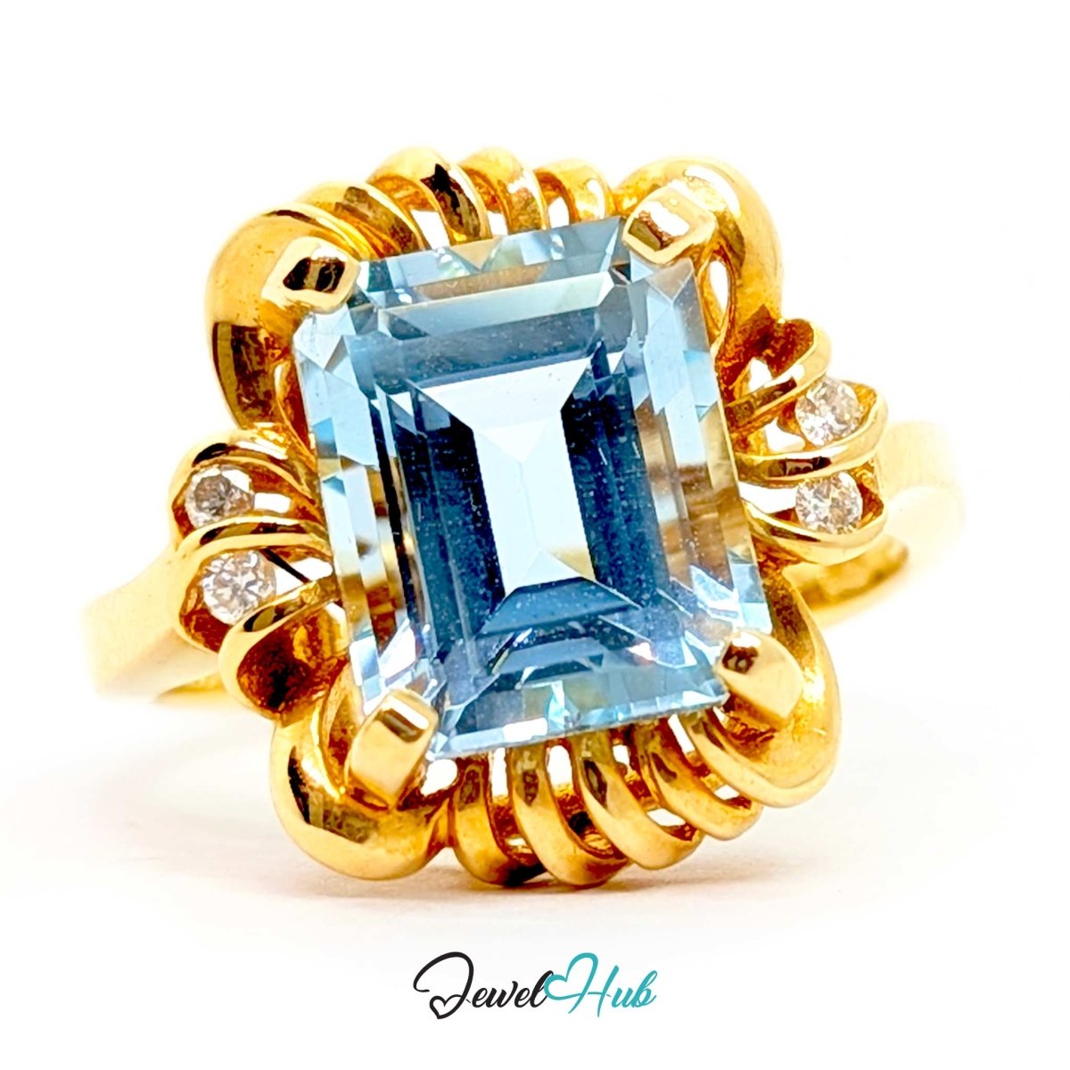 A 14k yellow gold ring featuring a large rectangular emerald-cut light blue gemstone as the center, accented by small round diamonds on the sides and a textured gold halo setting, shown on a white background with a 'JewelHub' watermark at the bottom.