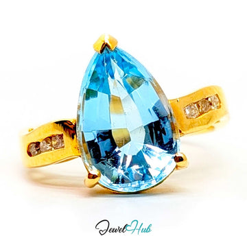 A 14k gold ring featuring a large pear-cut light blue gemstone in a prong setting, with small clear accent stones on the band, shown on a white background with a JewelHub watermark.