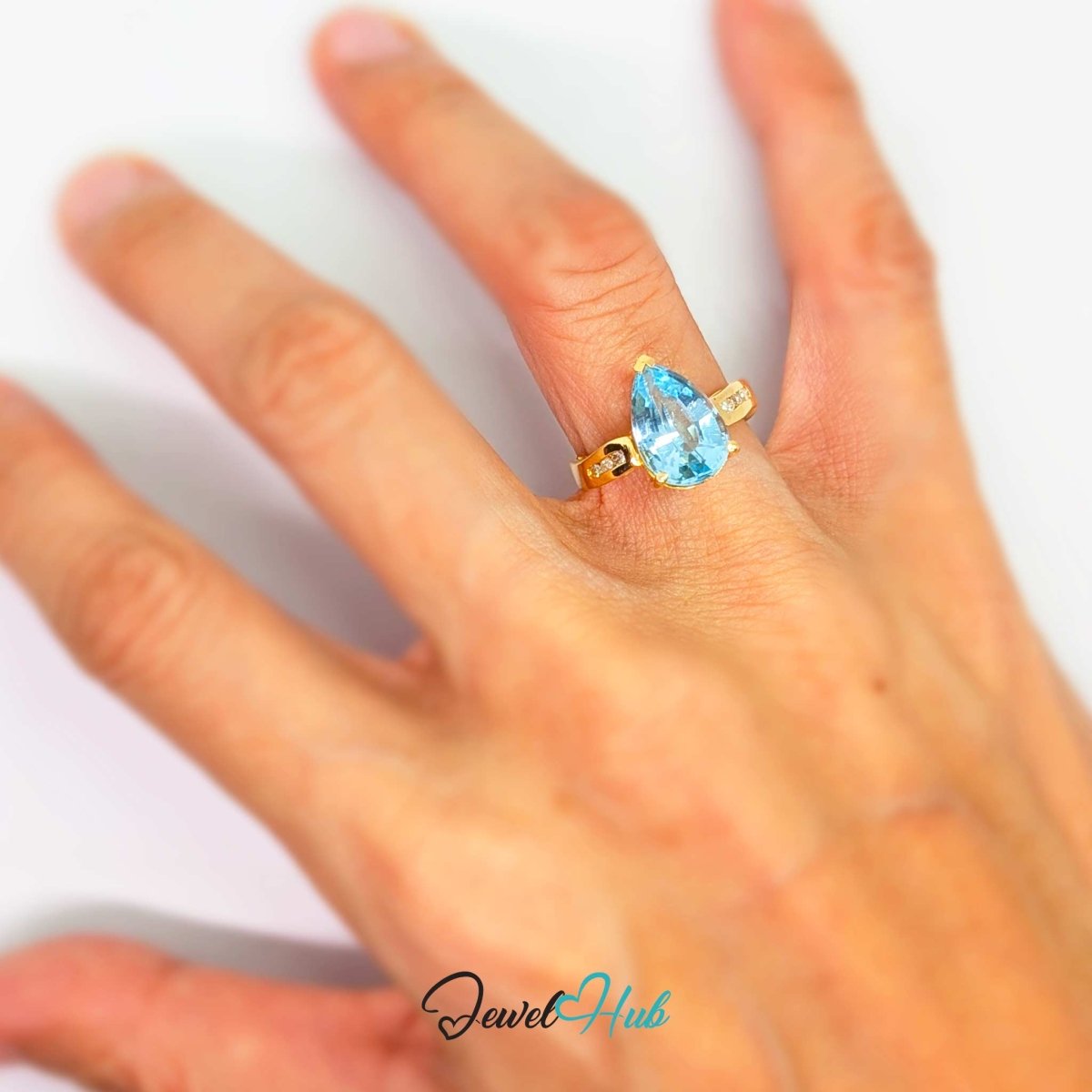 A 14k gold ring with a pear-cut light blue gemstone worn on a person's finger, shown against a plain white background with a 'JewelHub' watermark at the bottom.