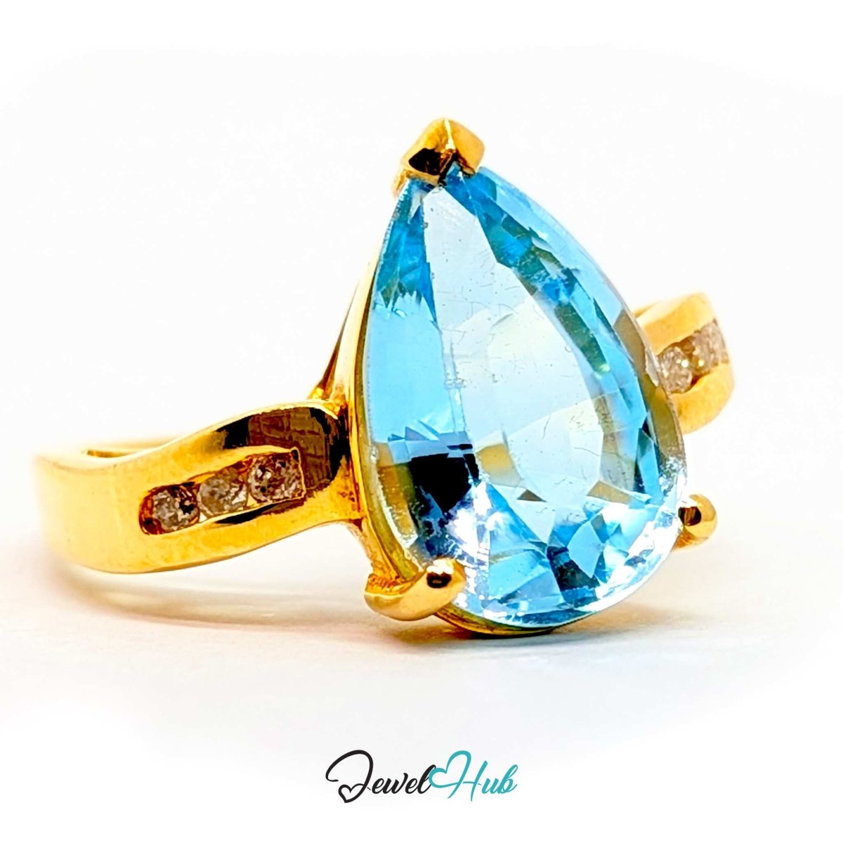 A 14k gold ring featuring a large teardrop-shaped light blue gemstone, with small clear accent stones on the band, shown on a white background with a JewelryHub watermark.