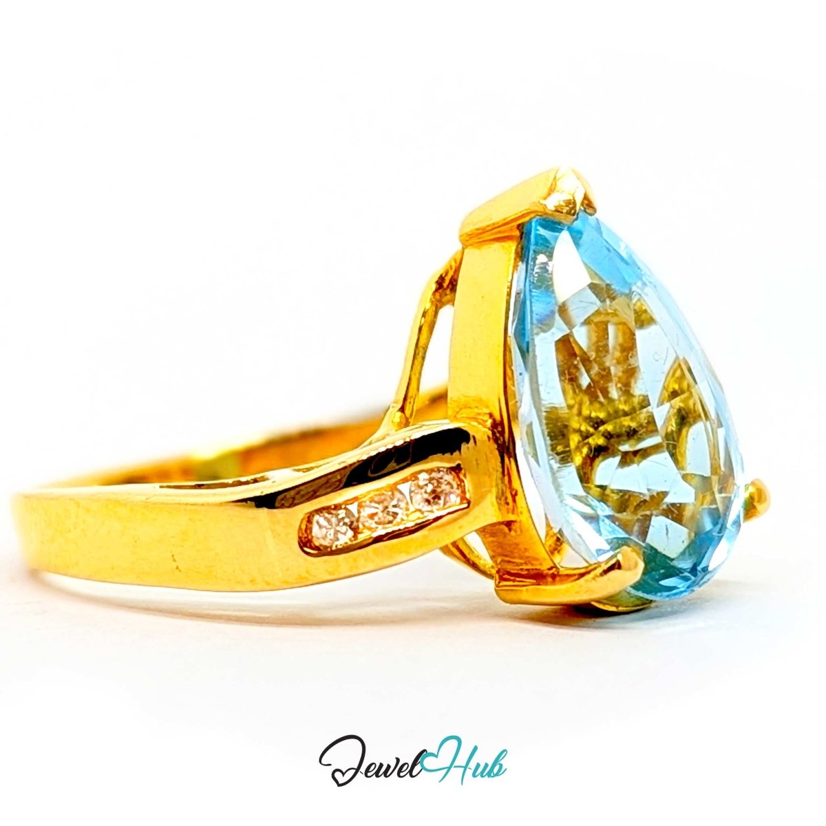 A 14k gold ring featuring a large teardrop-shaped light blue gemstone and a small row of clear stones on the band, shown on a white background with a JewelryHub watermark.