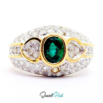 A 14k yellow gold ring featuring a central oval emerald green gemstone, flanked by two heart-shaped clear stones and a small round accent stone, all set in a pavé setting of clear stones. The ring is photographed on a white background with a 'JewelHub' watermark at the bottom.