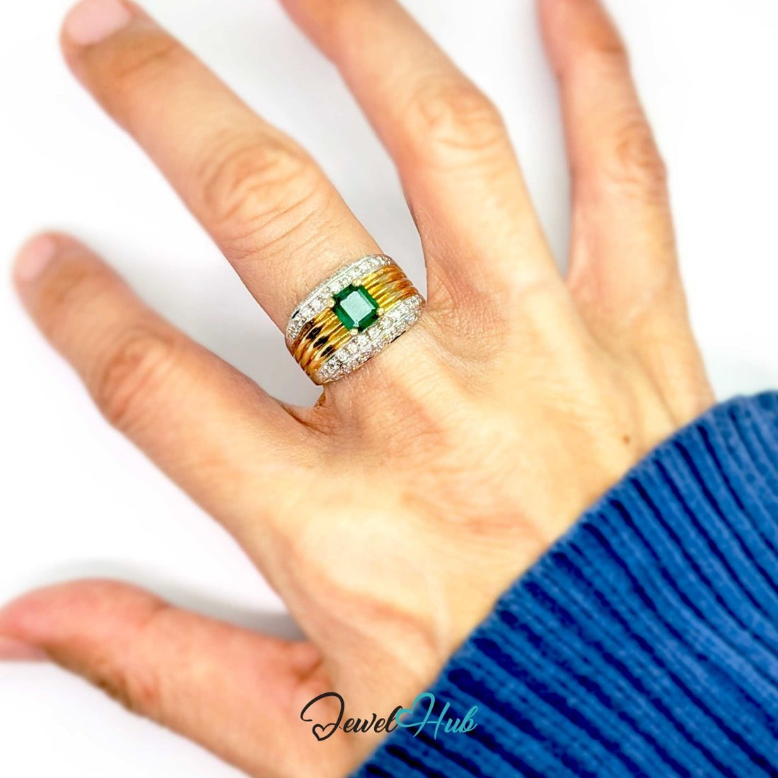 A wide 14k gold and silver band ring featuring a central green emerald-cut gemstone, surrounded by small clear stones along the top and bottom, with textured gold bars on either side of the center stone. The ring is photographed on a white background with a 'JewelHub' watermark at the bottom.