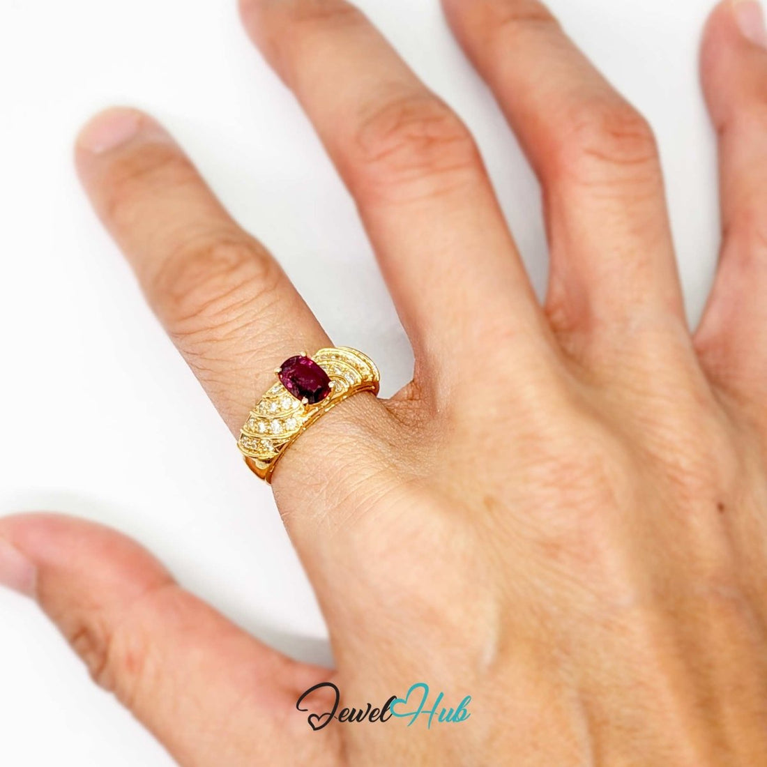 A yellow 14k gold ring featuring a large oval-cut pink gemstone in the center, surrounded by smaller clear stones and textured gold bands, shown on a white background with a JewelryHub watermark.