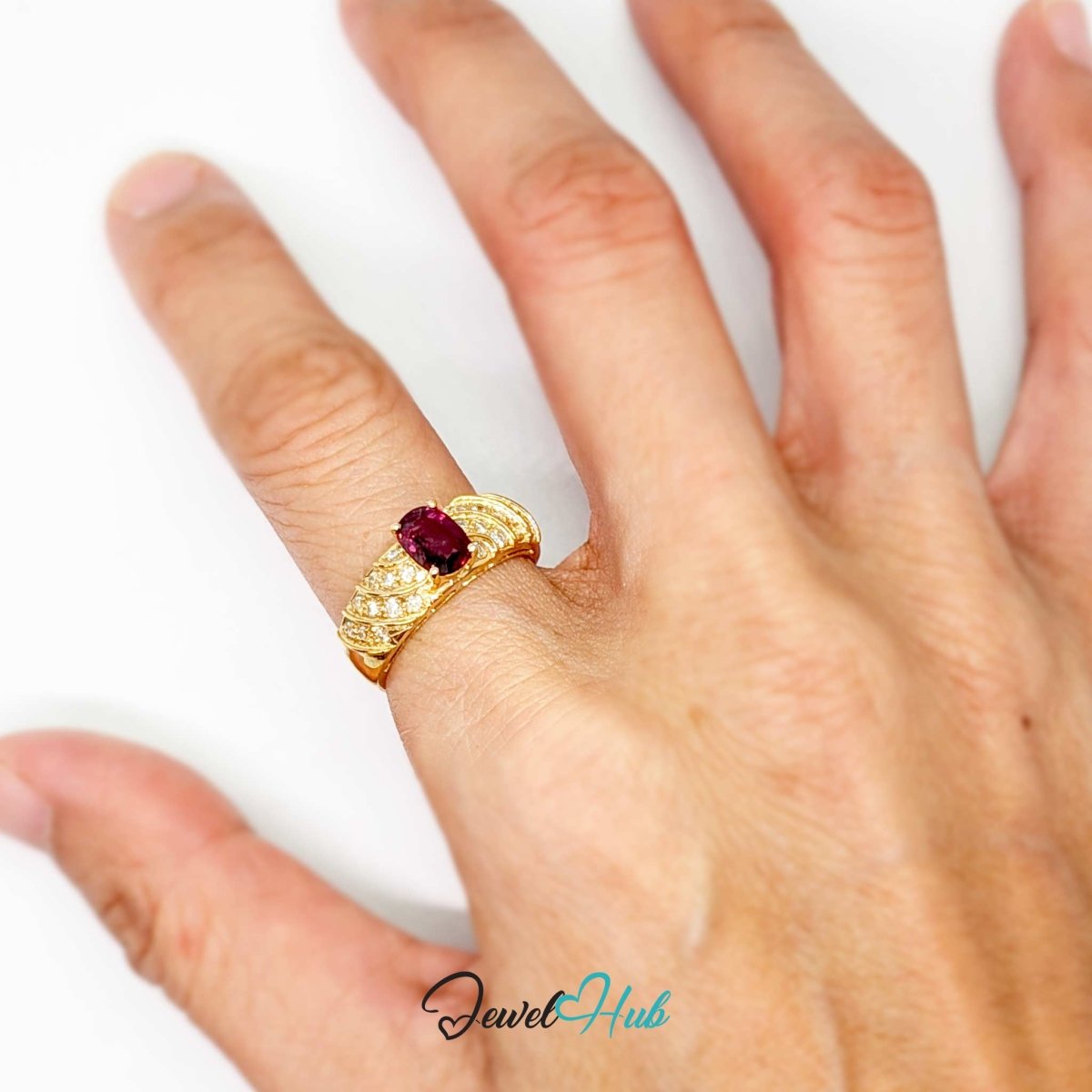A gold 14k ring with a central oval red gemstone and small clear stones on the band, shown worn on a person's finger against a plain white background.