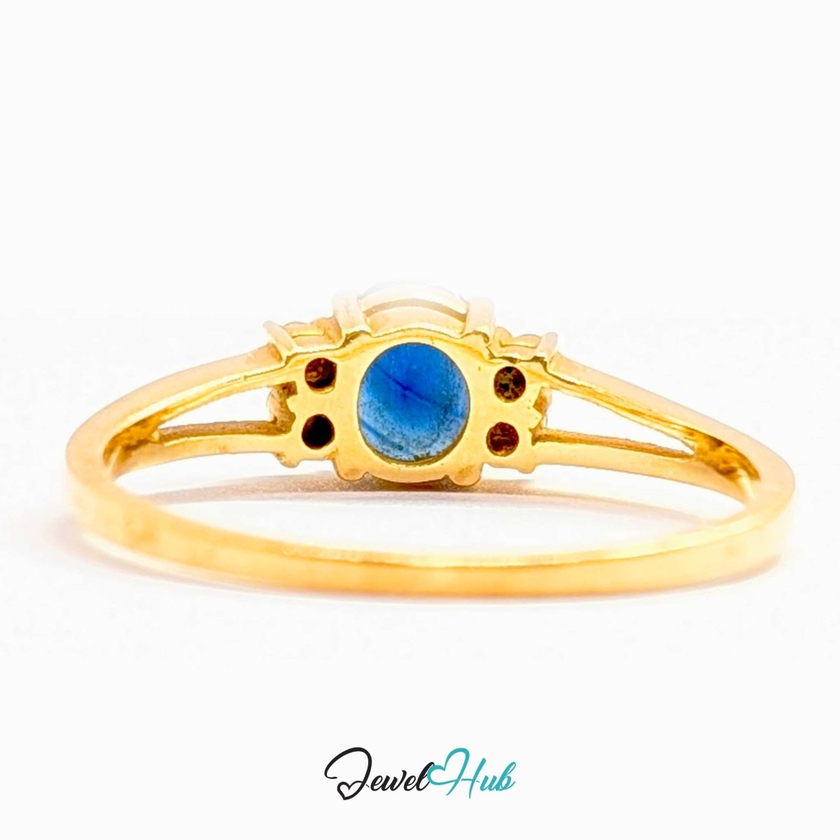 A 14k yellow gold ring featuring a central oval blue gemstone, accented by small round red gemstones on either side of the setting, shown against a plain white background.