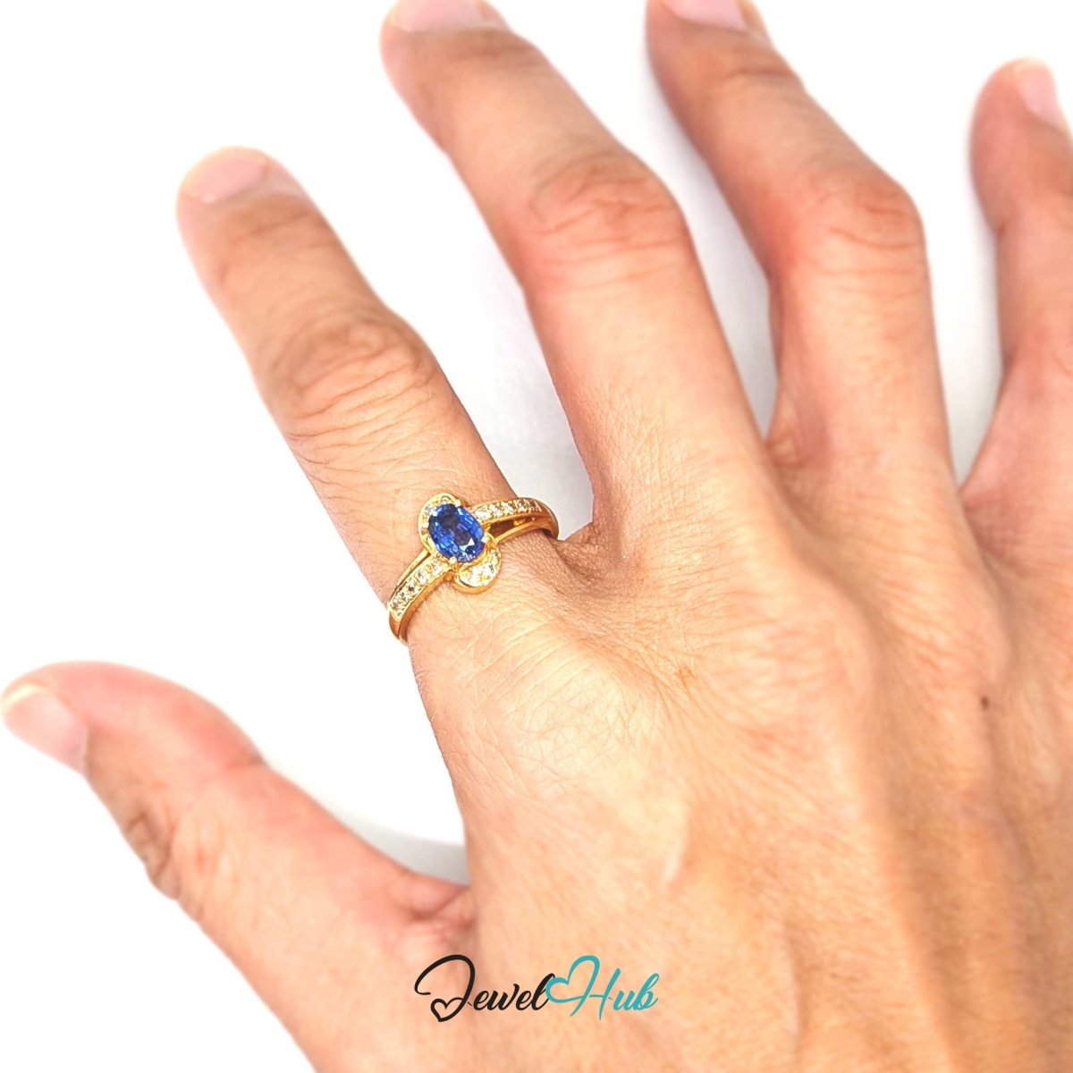 A 14k gold ring with a blue oval gemstone and small clear accent stones, shown worn on a person's finger against a plain white background. The brand name 'JewelHub' is visible as a watermark at the bottom.