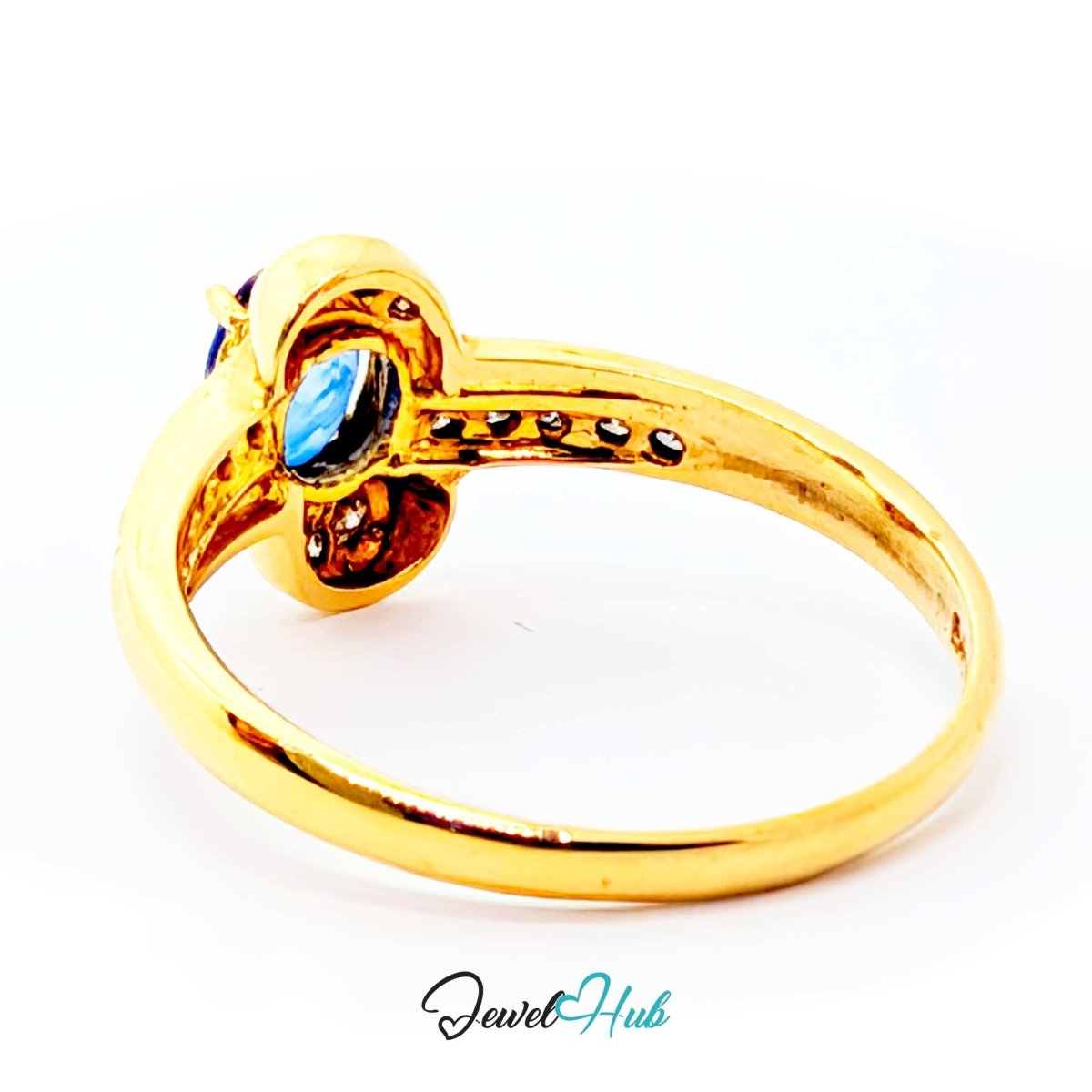 A gold 14k ring with a decorative floral or scroll motif, featuring a central blue oval gemstone and small dark accent stones, shown on a white background with a JewelHub watermark.