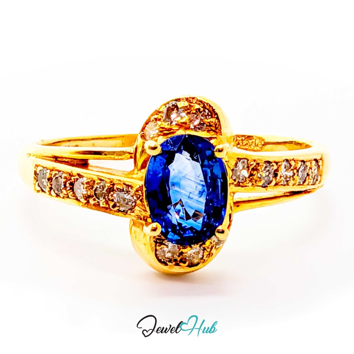 A 14k yellow gold ring featuring an oval-cut blue sapphire center stone, surrounded by small round diamonds on the shoulders and a channel-set row of diamonds along the split band. The ring is photographed on a clean white background with a 'JewelHub' watermark at the bottom.