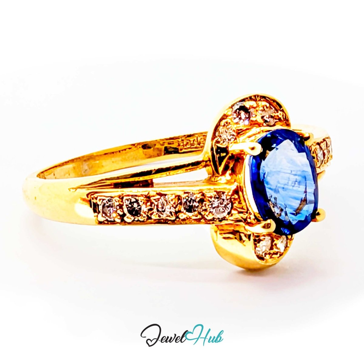 A 14k yellow gold ring featuring a large oval blue gemstone in a prong setting, accented with small round clear stones along the band, shown on a white background with a JewelHub watermark.