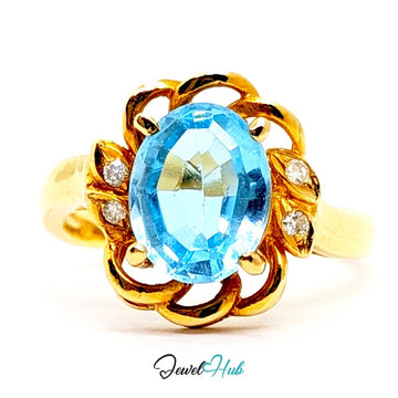 A yellow 14k gold ring featuring an oval-cut light blue topaz center stone and small round diamond accents on the sides, set against a plain white background with a 'JewelHub' watermark at the bottom.