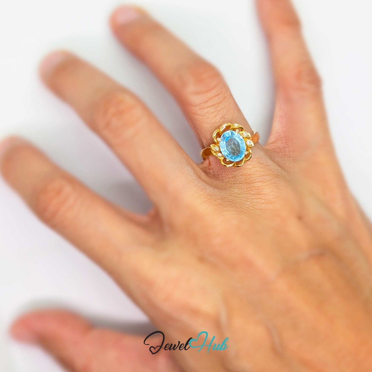 A 14k gold ring with an oval light blue gemstone, worn on a person's finger against a plain white background.