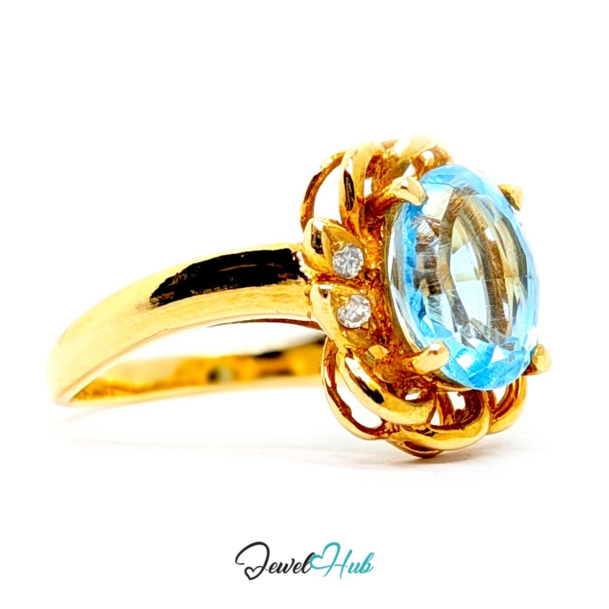 A 14k yellow gold ring featuring an oval-cut light blue topaz gemstone and two small round-cut diamonds, set in an ornate floral-like halo on a white background with a 'JewelHub' watermark at the bottom.