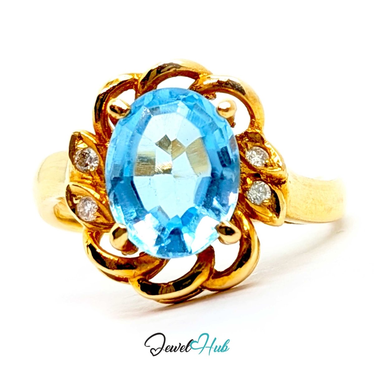 A 14k yellow gold ring featuring an oval-cut light blue topaz center stone and small clear accent stones, shown on a white background with a JewelHub watermark.