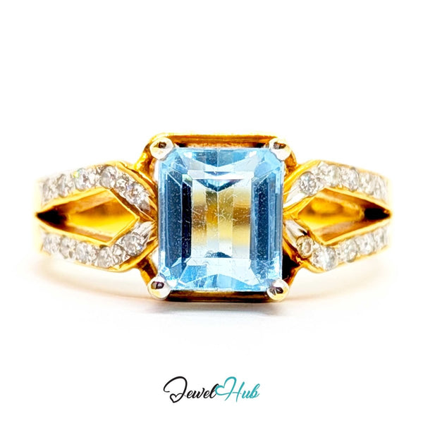 A 18k yellow gold ring featuring a large rectangular emerald-cut light blue gemstone in the center, flanked by pavé-set clear stones on the band and a gold setting.