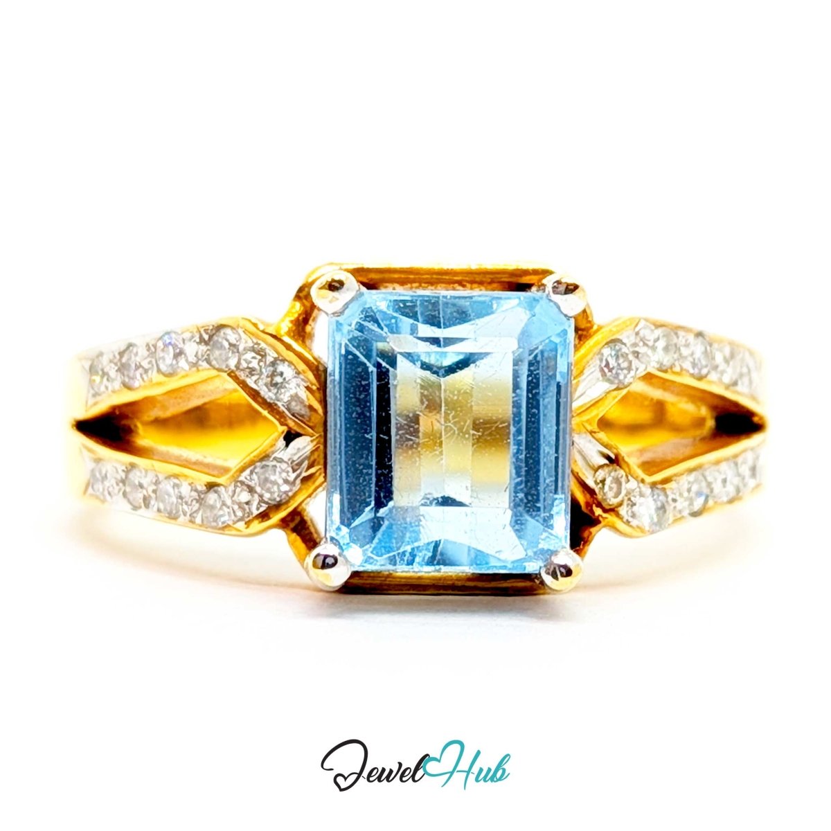 A 18k yellow gold ring featuring a large rectangular blue topaz center stone and pavé-set clear accent stones along the split shank, shown on a white background with a JewelryHub watermark.
