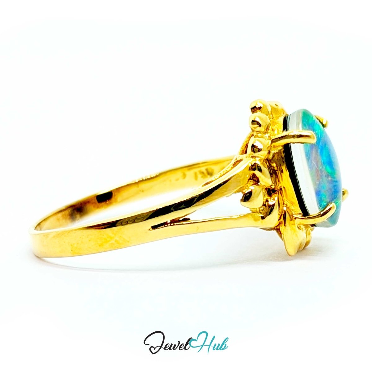 A 18k yellow gold ring featuring an oval-cut iridescent opal stone with blue, green, and white flashes, set in a decorative floral crown-like halo. The ring is photographed on a clean white background with a 'JewelHub' watermark at the bottom.