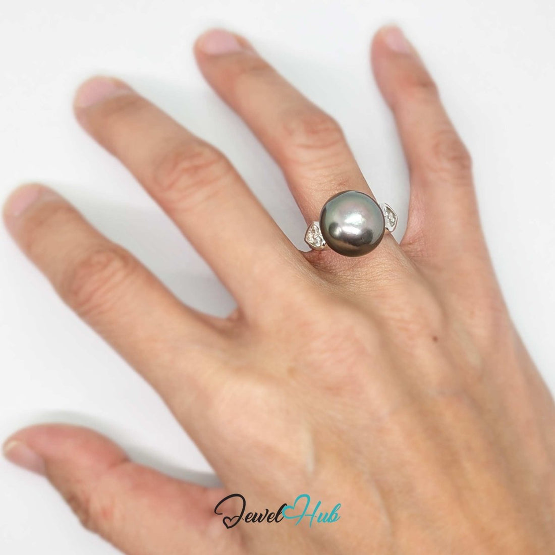 A round dark gray pearl ring with a 18k white gold  setting featuring small clear stones on each side, shown on a white background with a JewelryHub watermark.