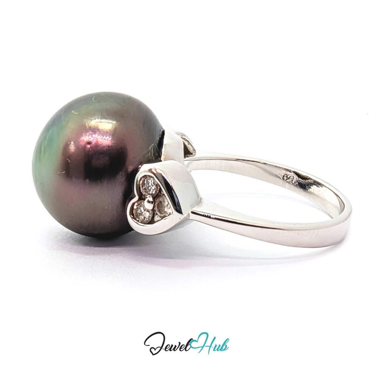 A 18k white gold  ring featuring a large, round, iridescent dark pearl and a small heart-shaped cluster of clear stones on the band, set against a plain white background.