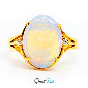 A 18k yellow gold ring featuring a large oval cabochon opal with iridescent white, blue, and yellow flashes, accented by two small round-cut diamonds on the shoulders, set against a plain white background.