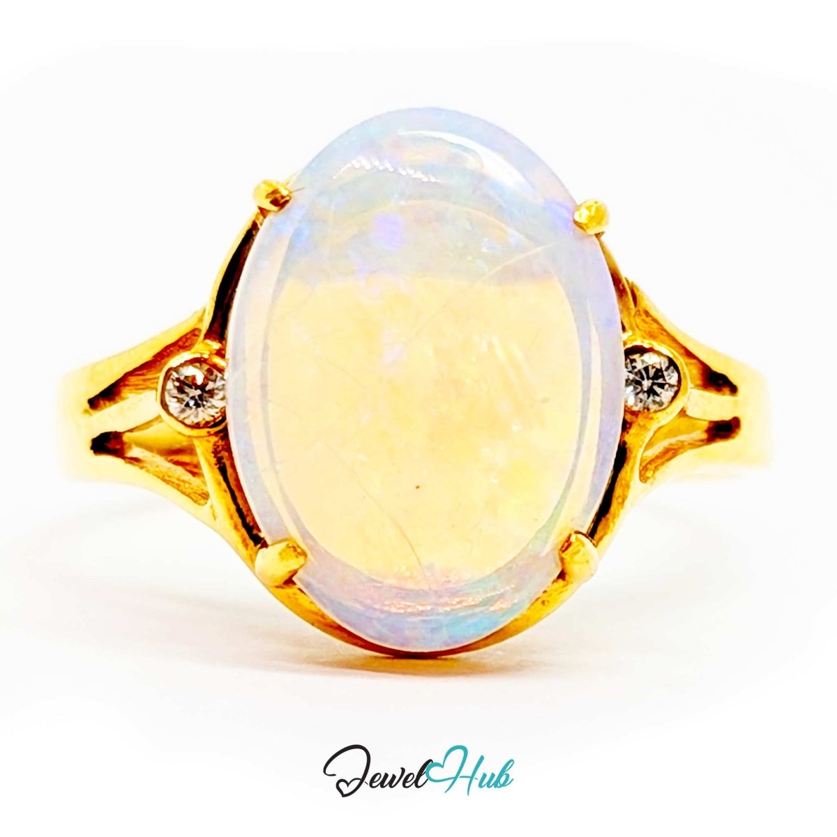 A 18k gold ring featuring a large oval cabochon opal with iridescent white, blue, and soft yellow tones, accented by two small clear stones on the band, shown on a white background with a 'JewelHub' watermark.