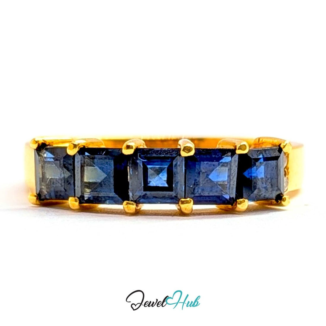 A yellow gold ring featuring five square-cut dark blue sapphires in a row, set against a plain white background with a 'JewelHub' watermark at the bottom.