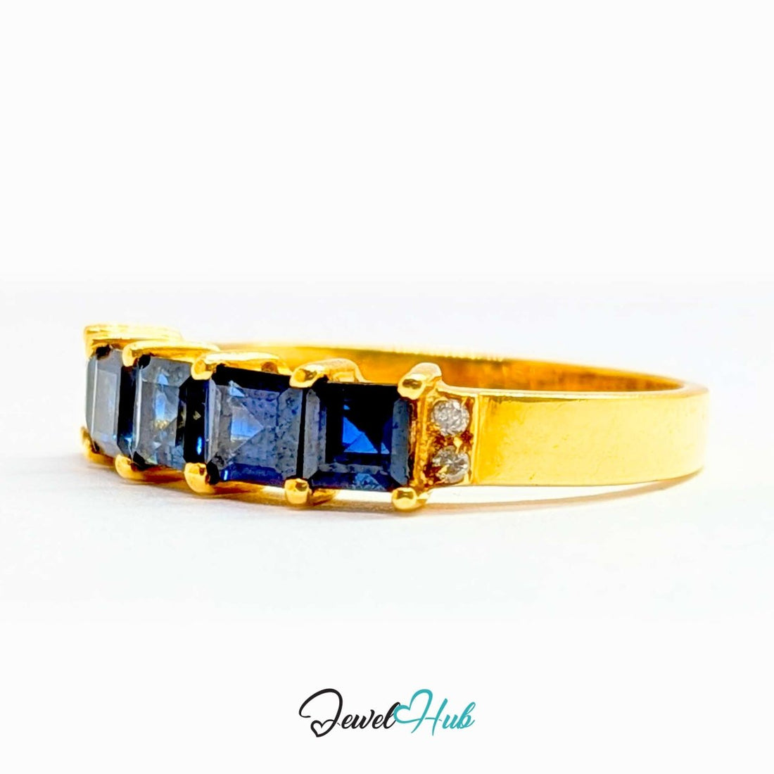 A yellow gold ring featuring five square-cut dark blue sapphires in a row, set against a plain white background with a 'JewelHub' watermark at the bottom.