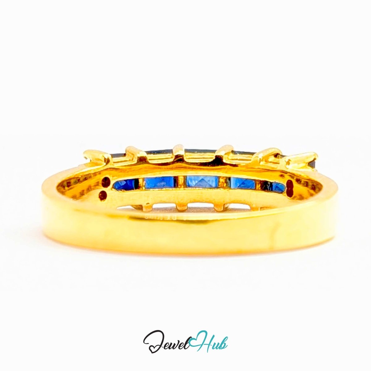 A 18k gold eternity-style ring with a channel setting featuring blue stones and small sapphire stones, shown on a white background with a 'JewelHub' watermark at the bottom.