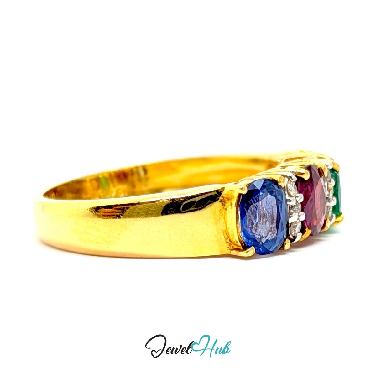 A 18k yellow gold ring featuring a row of colorful gemstones, including a prominent oval blue sapphire, a round pinkish-red ruby, and smaller green and clear stones, shown on a white background with a 'JewelHub' watermark.
