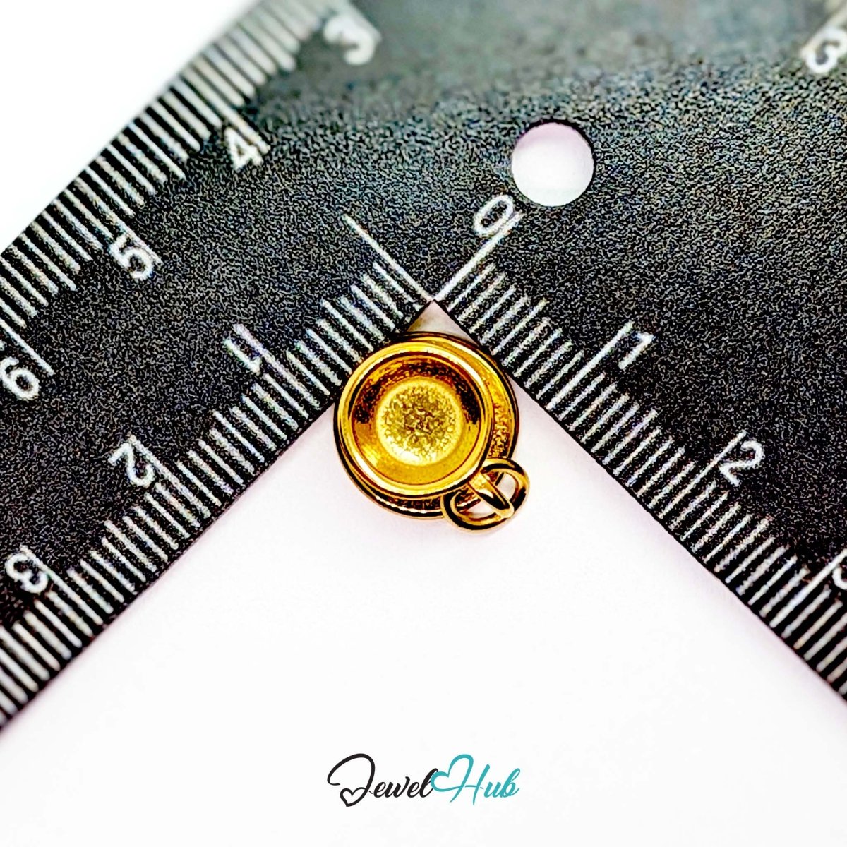 Three-dimensional coffee cup and saucer charm in gold stainless steel - beside a ruler for scale - JewelHub