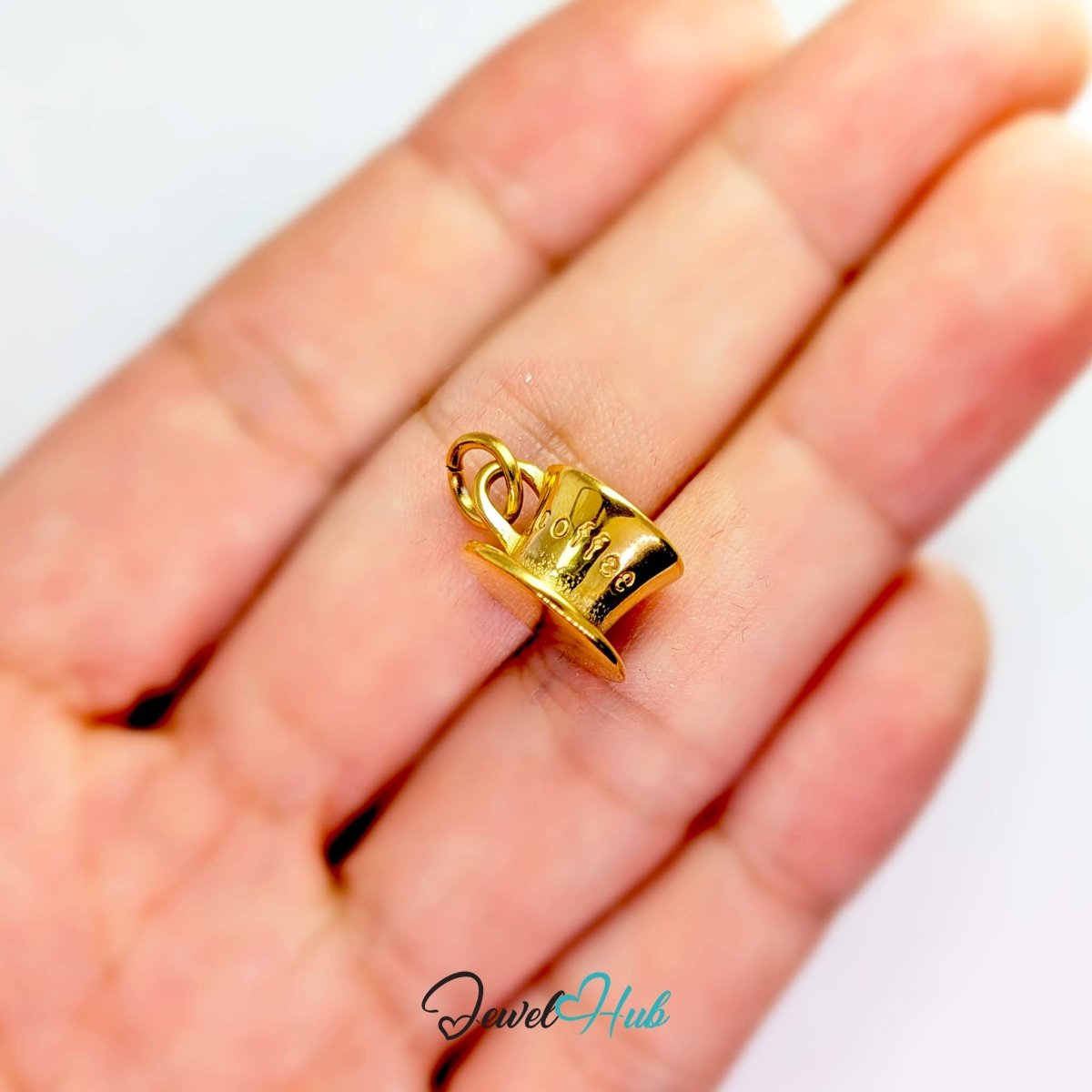Three-dimensional coffee cup and saucer charm in gold stainless steel - held in the hand for scale - JewelHub
