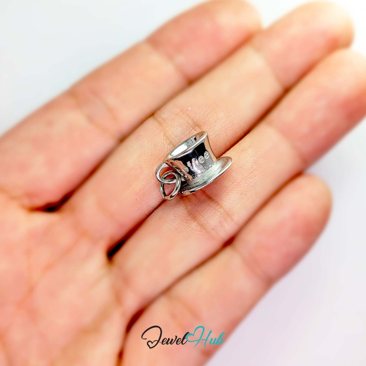 Three-dimensional coffee cup and saucer charm in silver stainless steel - held in the hand for scale - JewelHub