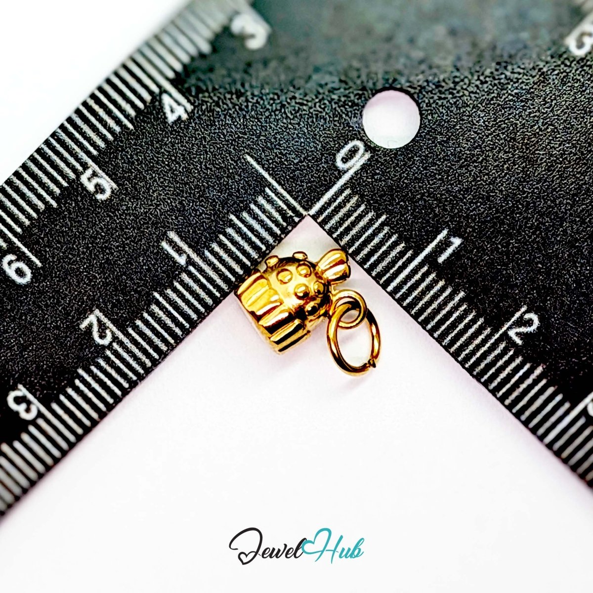 Three-dimensional cupcake charm in gold stainless steel - beside a ruler for scale - JewelHub