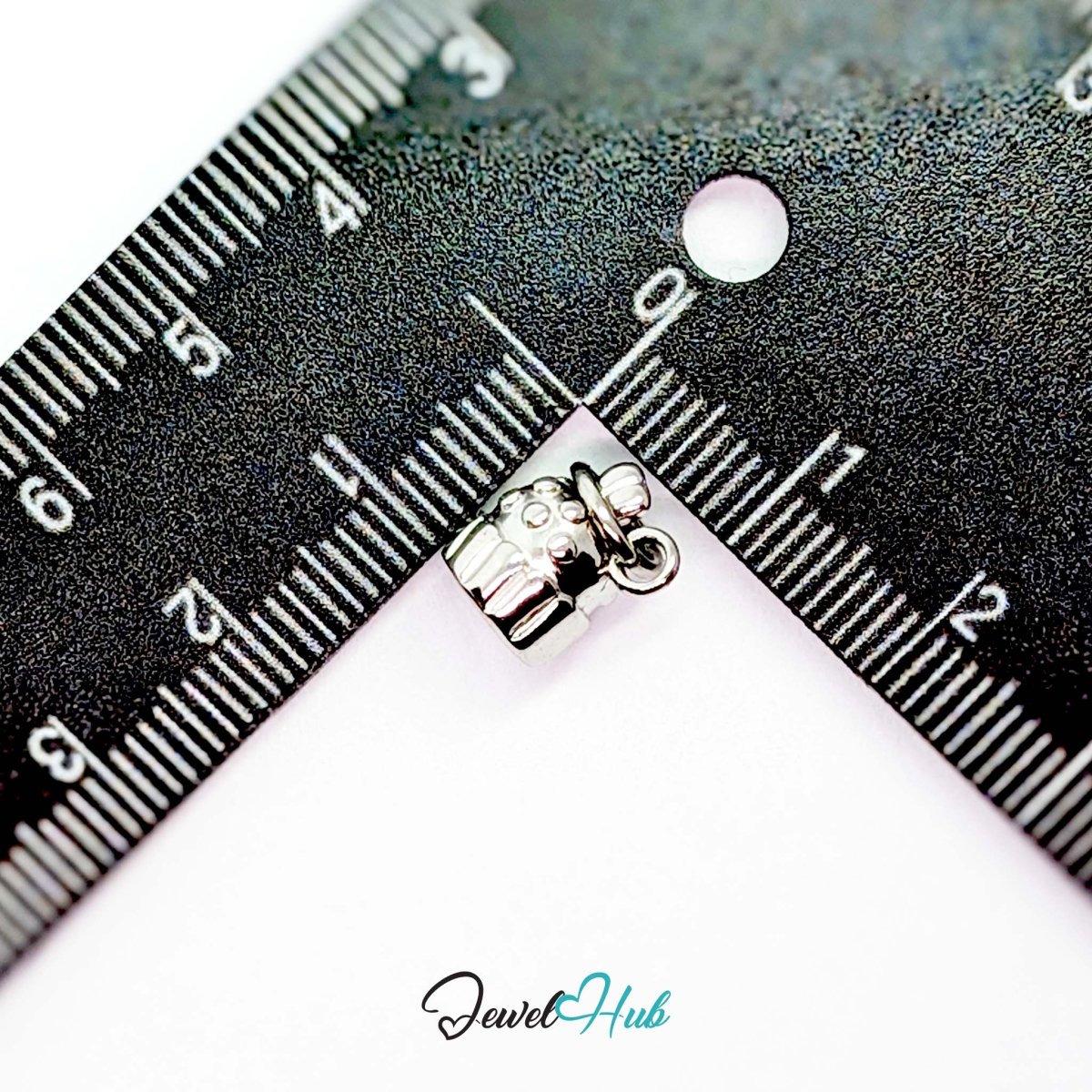 Three-dimensional cupcake charm in silver stainless steel - beside a ruler for scale - JewelHub