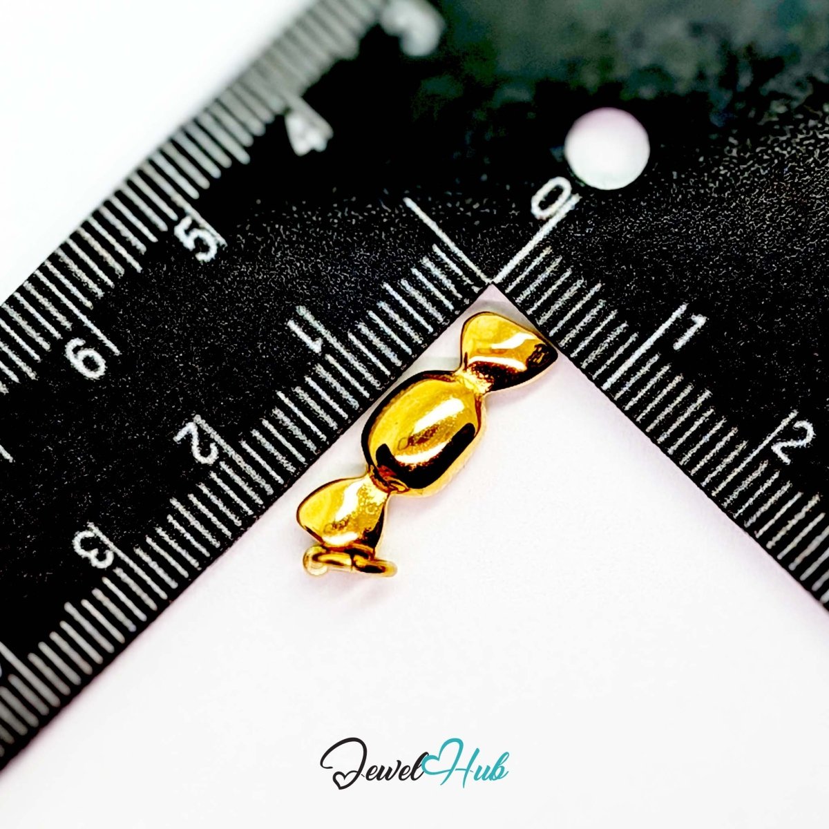 Wrapped sweet charm in gold stainless steel - beside a ruler for scale - JewelHub