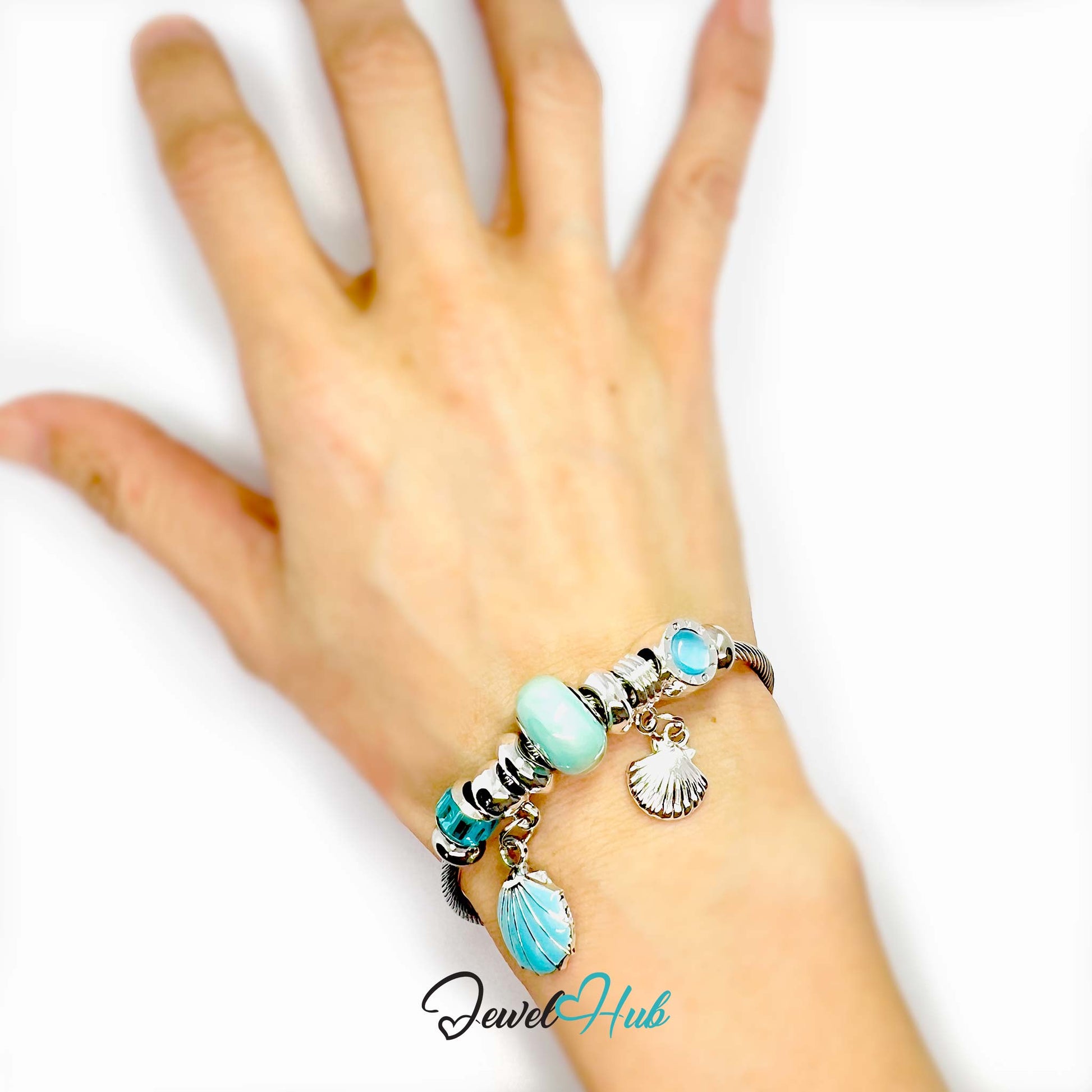 Hand wearing a bracelet with turquoise beads and charms on a white background, featuring the brand 'Jewel Hub'.