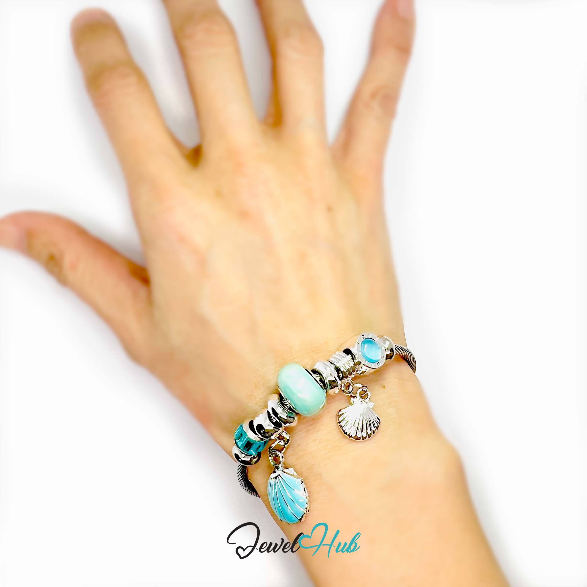 Hand wearing a bracelet with turquoise beads and charms on a white background, featuring the brand 'Jewel Hub'.