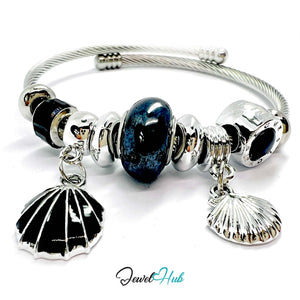Silver bracelet with black and silver shell charms and a blue heart bead on a white background.