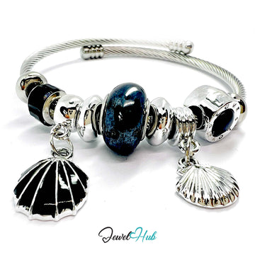 Silver bracelet with black and silver shell charms and a blue heart bead on a white background.