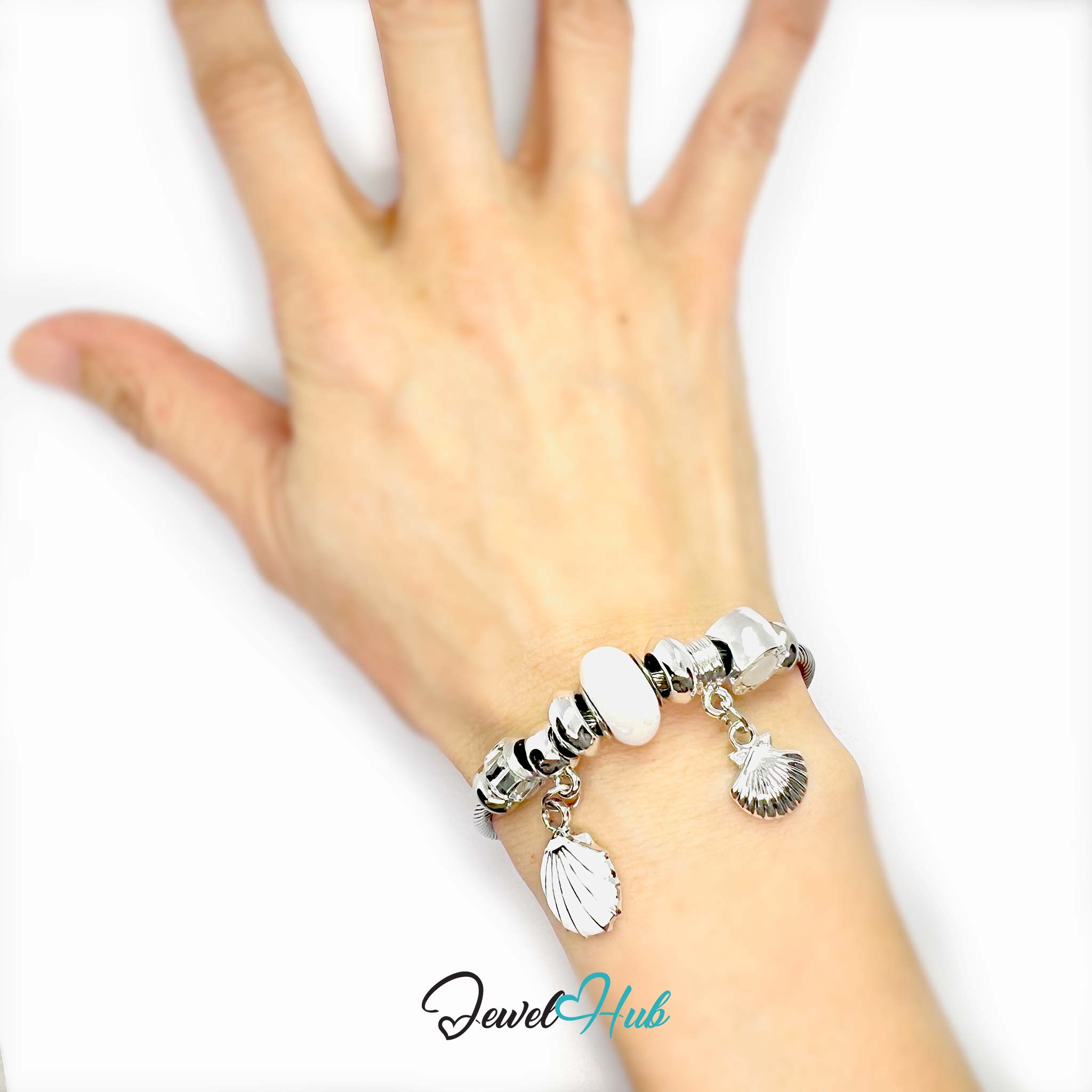 Hand wearing a silver bracelet with shell charms on a white background, branded 'Jewel Hub'.