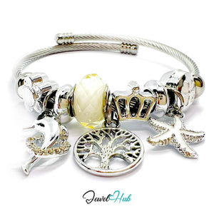 Silver bracelet with various charms including a yellow bead, crown, tree, and starfish on a white background. Brand 'Jewel Hub' visible.