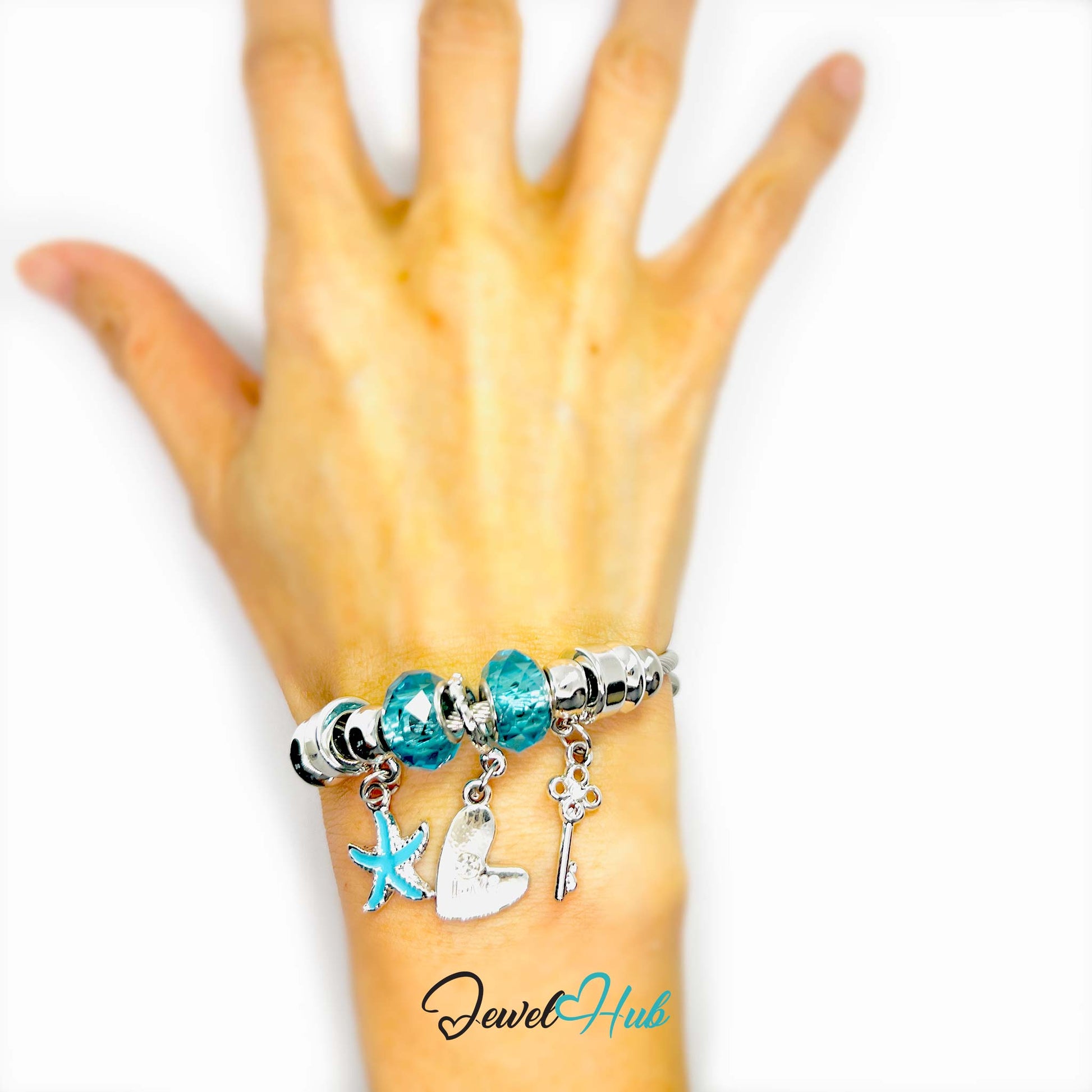 Hand wearing a bracelet with charms on a white background, featuring the brand 'Jewel Hub'.
