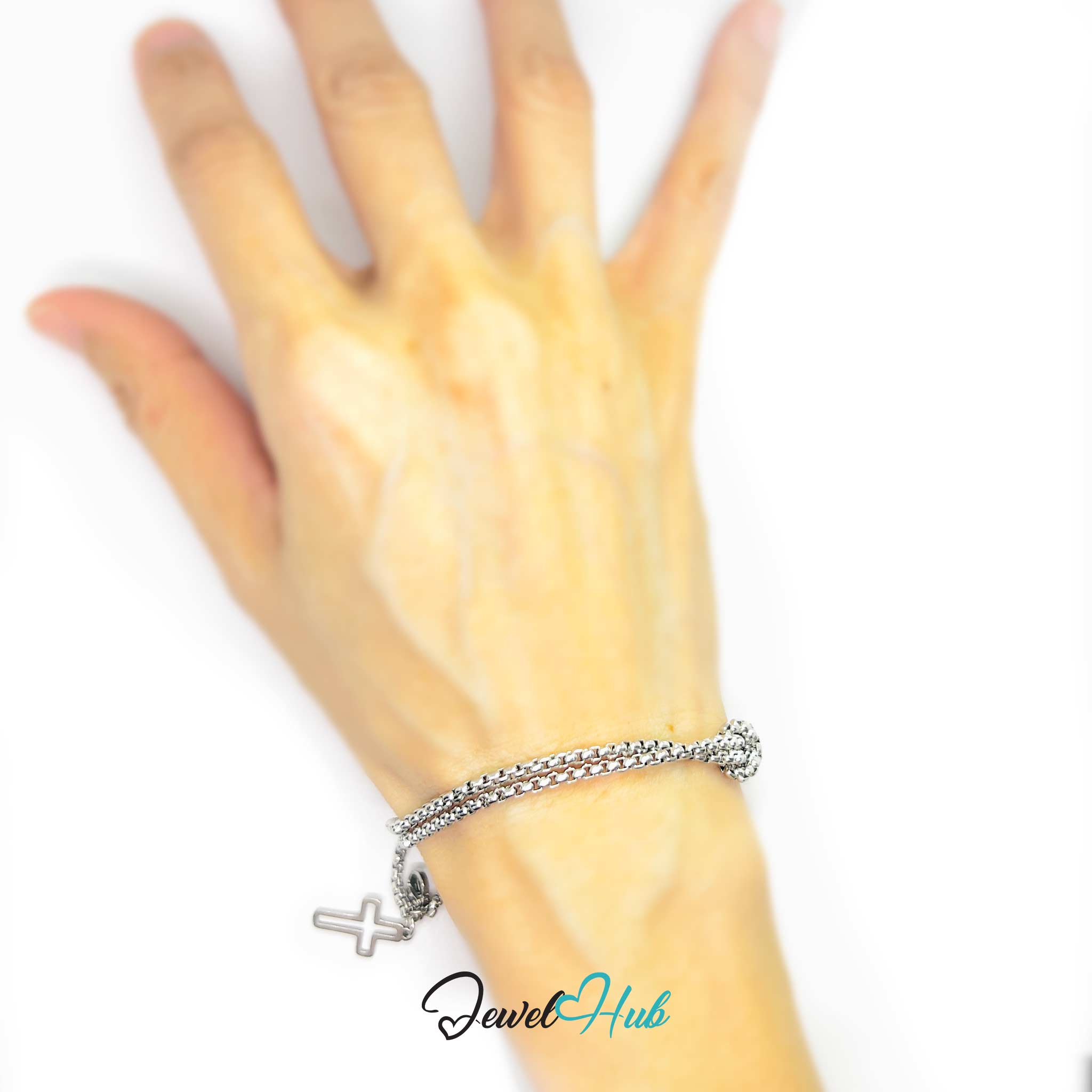 Hand wearing a silver bracelet with a cross charm on a white background, branded 'Jewel Hub'.