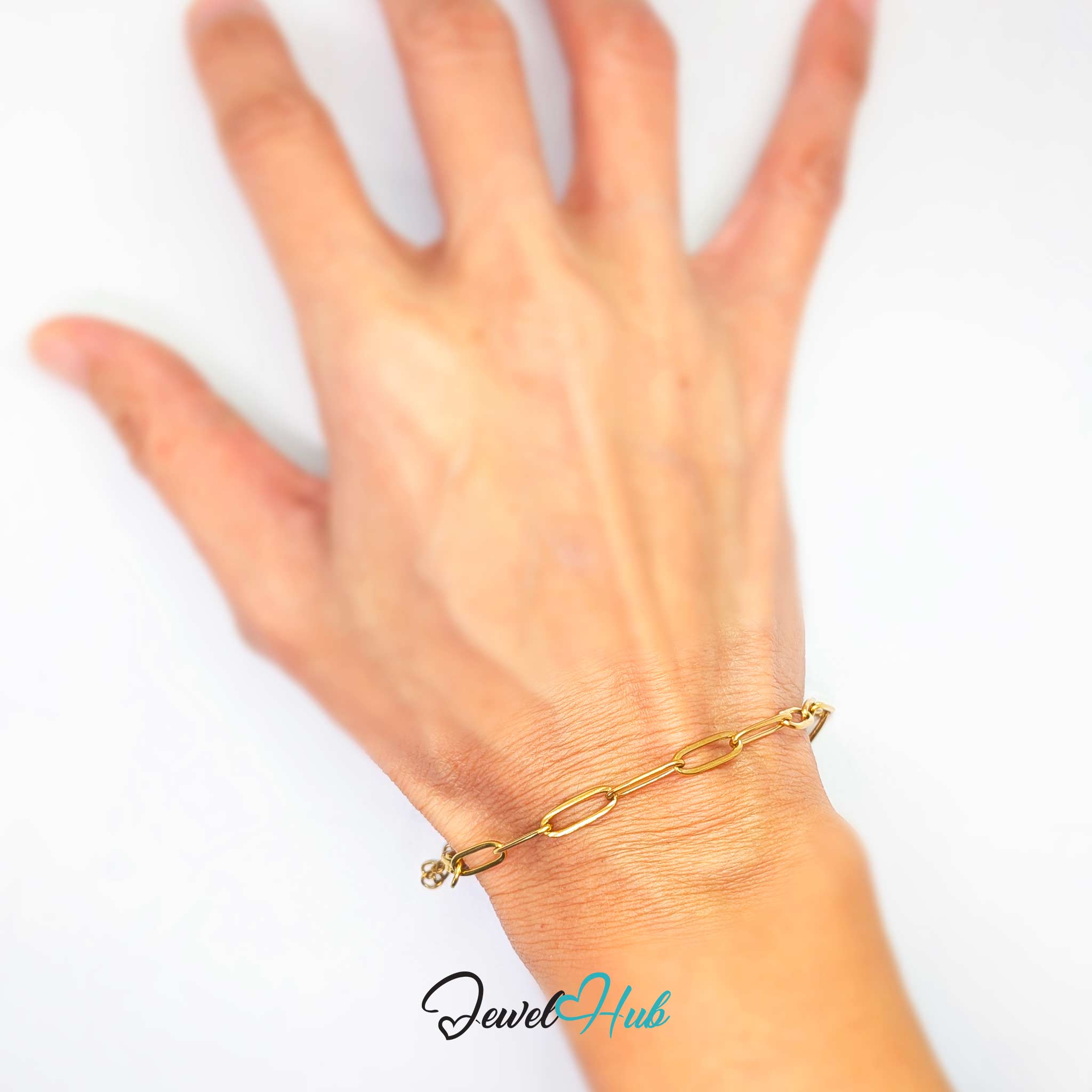 A close-up of a person's hand and wrist wearing a delicate gold paperclip chain bracelet against a plain white background.