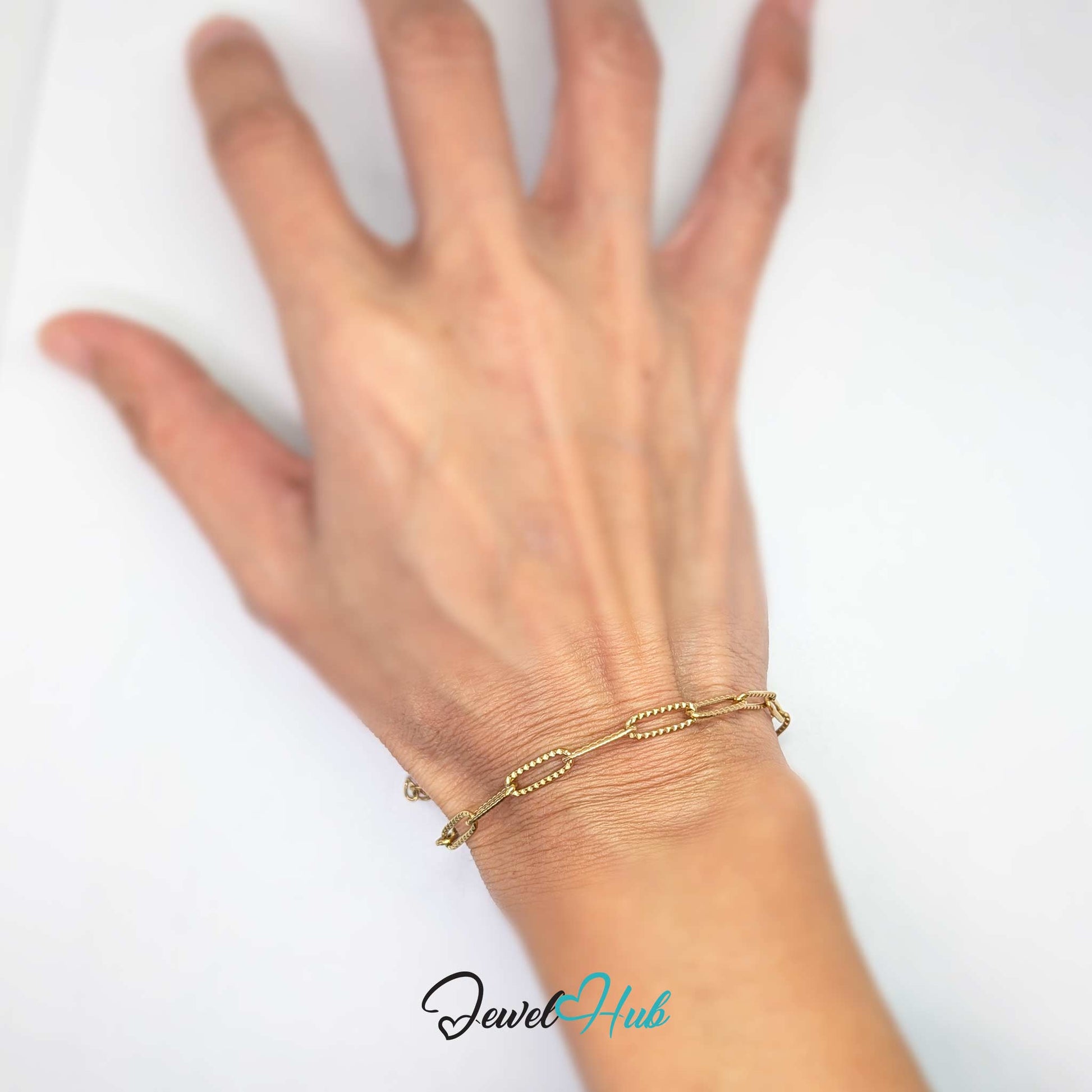 A delicate gold chain bracelet with small bead links worn on a person's wrist, shown against a plain white background with a 'JewelHub' watermark at the bottom.
