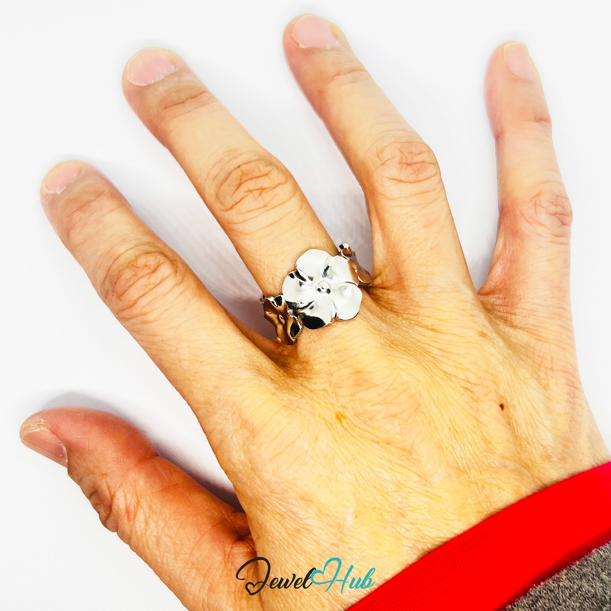 Hand wearing a silver ring with a flower design on a white background, featuring 'Jewel Hub' branding.