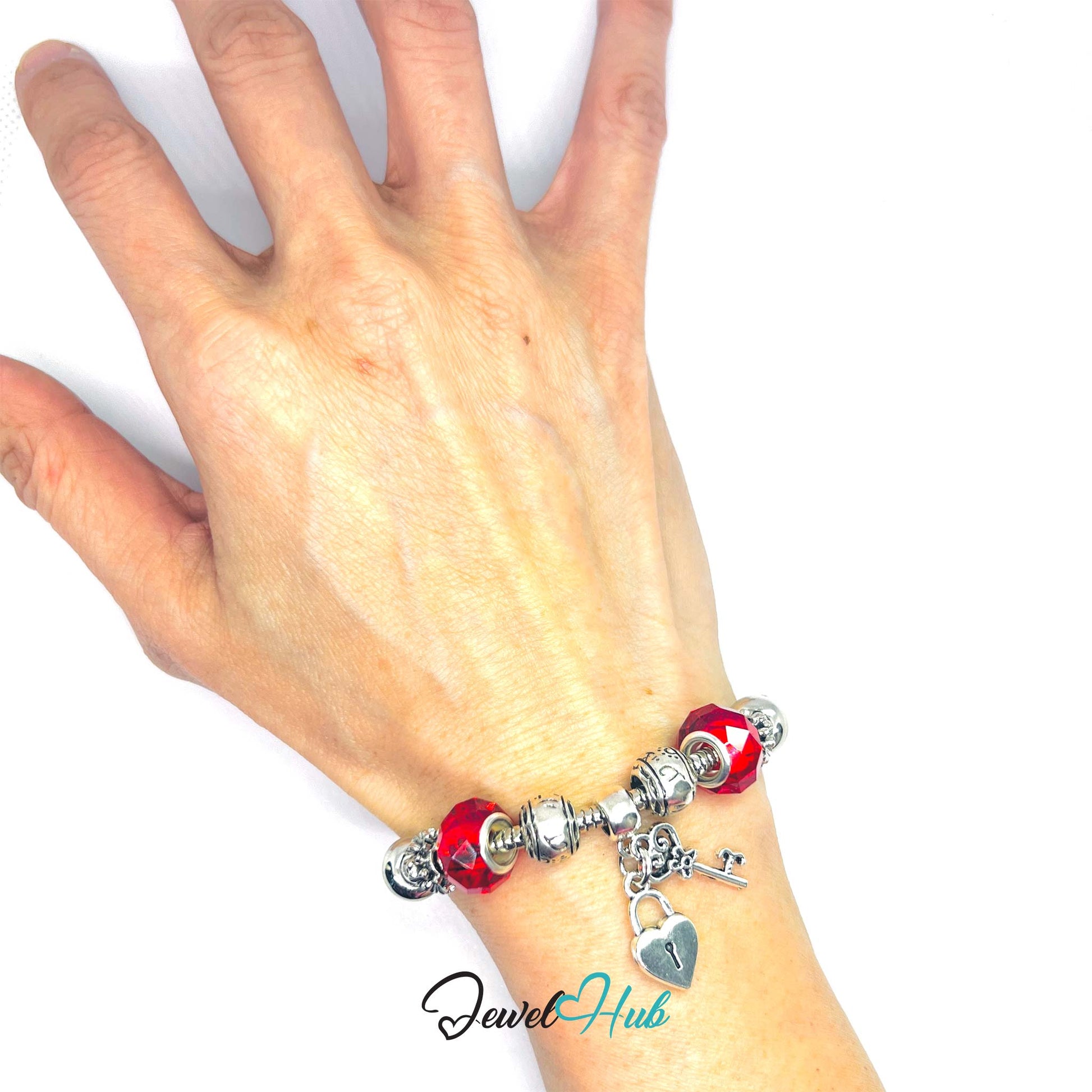 Hand wearing a bracelet with red beads and a heart lock charm on a white background, branded 'Jewel Hub'.