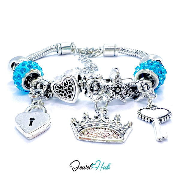 Silver bracelet with various charms including a blue bead, heart, lock, crown, and cloud on a white background. Brand 'Jewel Hub' visible.